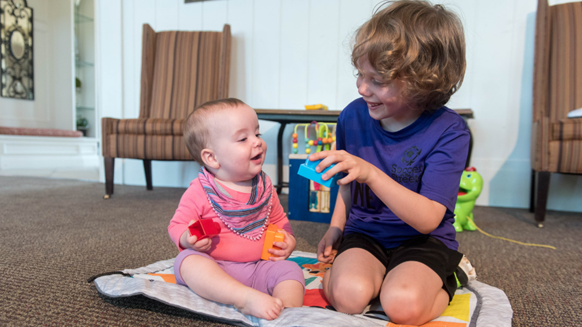older brother holding toy to show baby sister