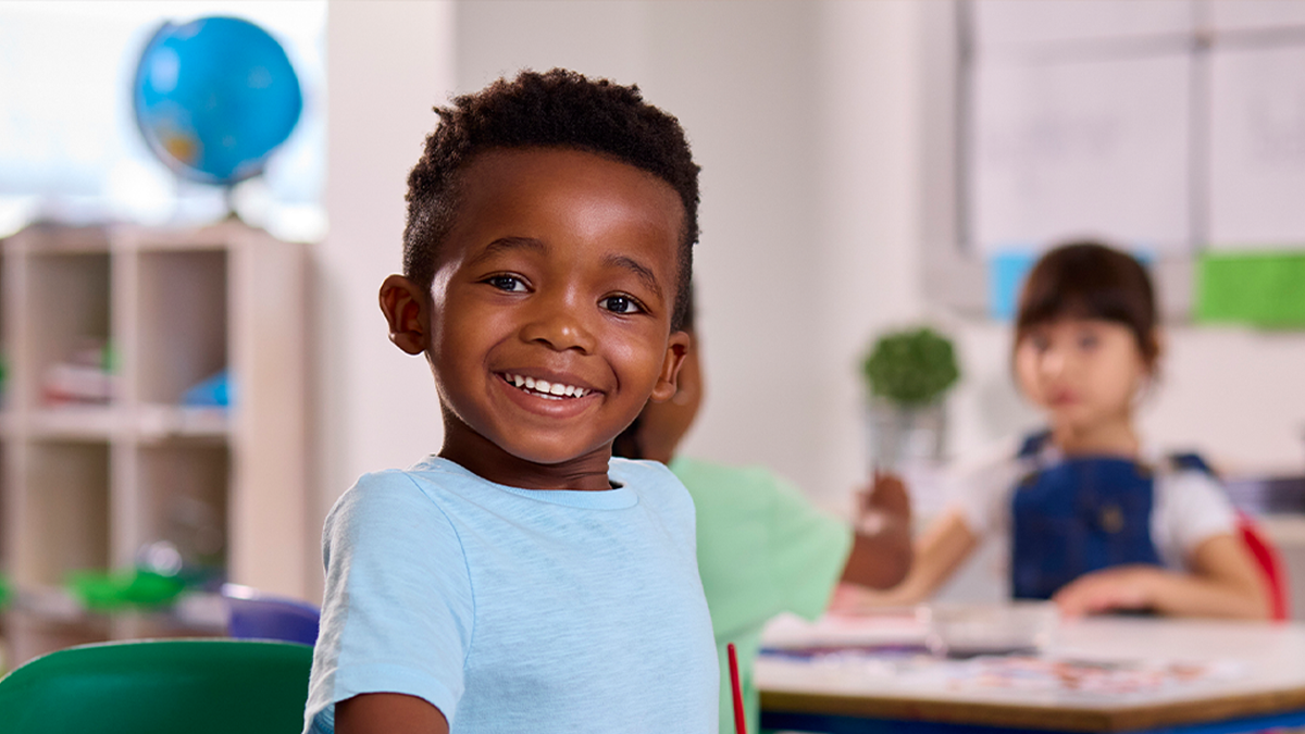 Child sitting int he classroom looking at the camera and smiling.