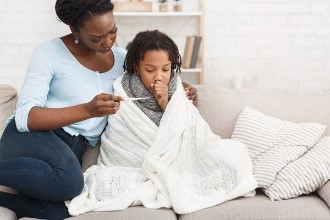 Una madre abrazando a su hijo enfermo y mirando el termómetro.