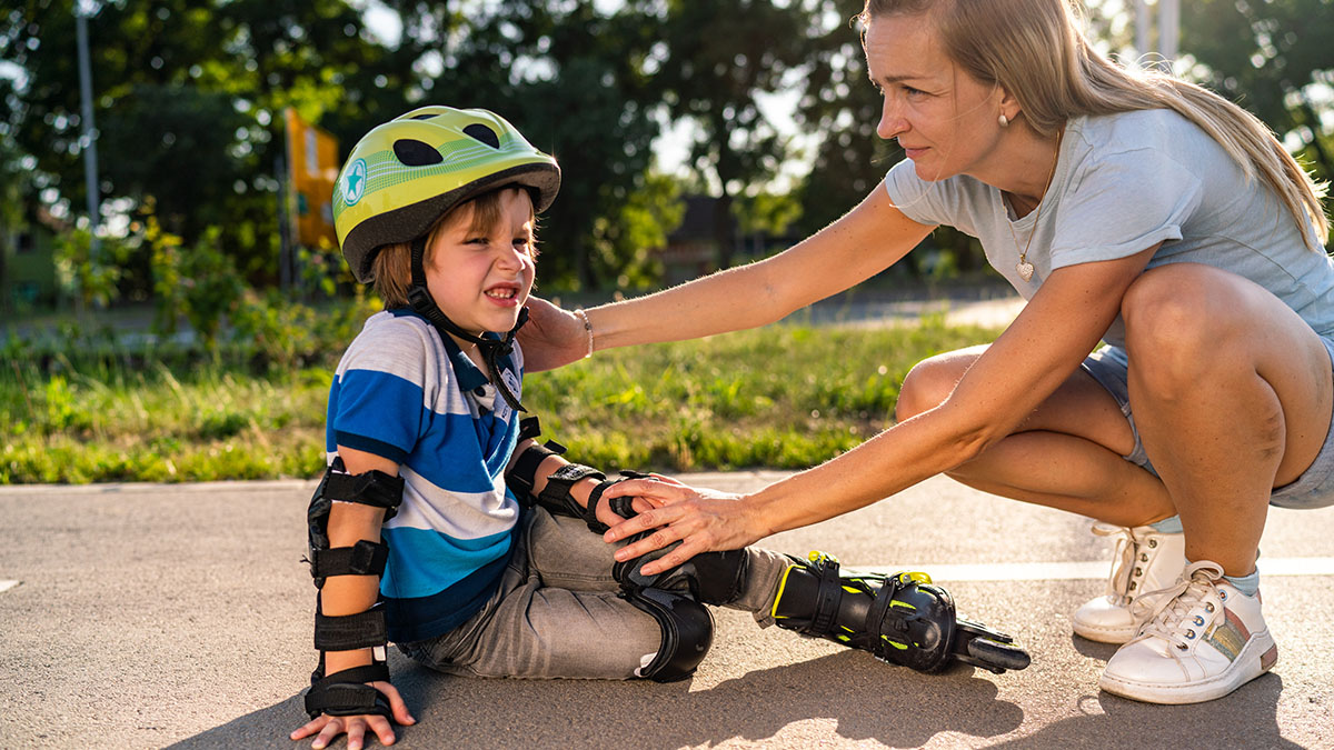 Mom helping son who fell while rollerblading.