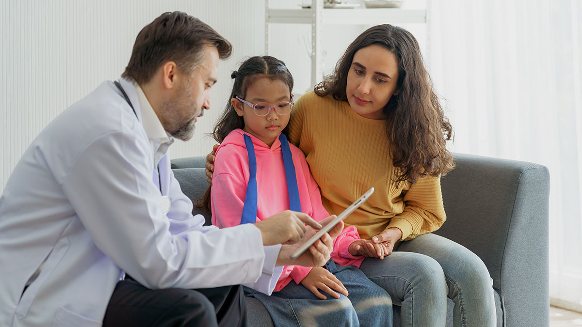 Doctor sitting on couch with mother and daughter going over chart.