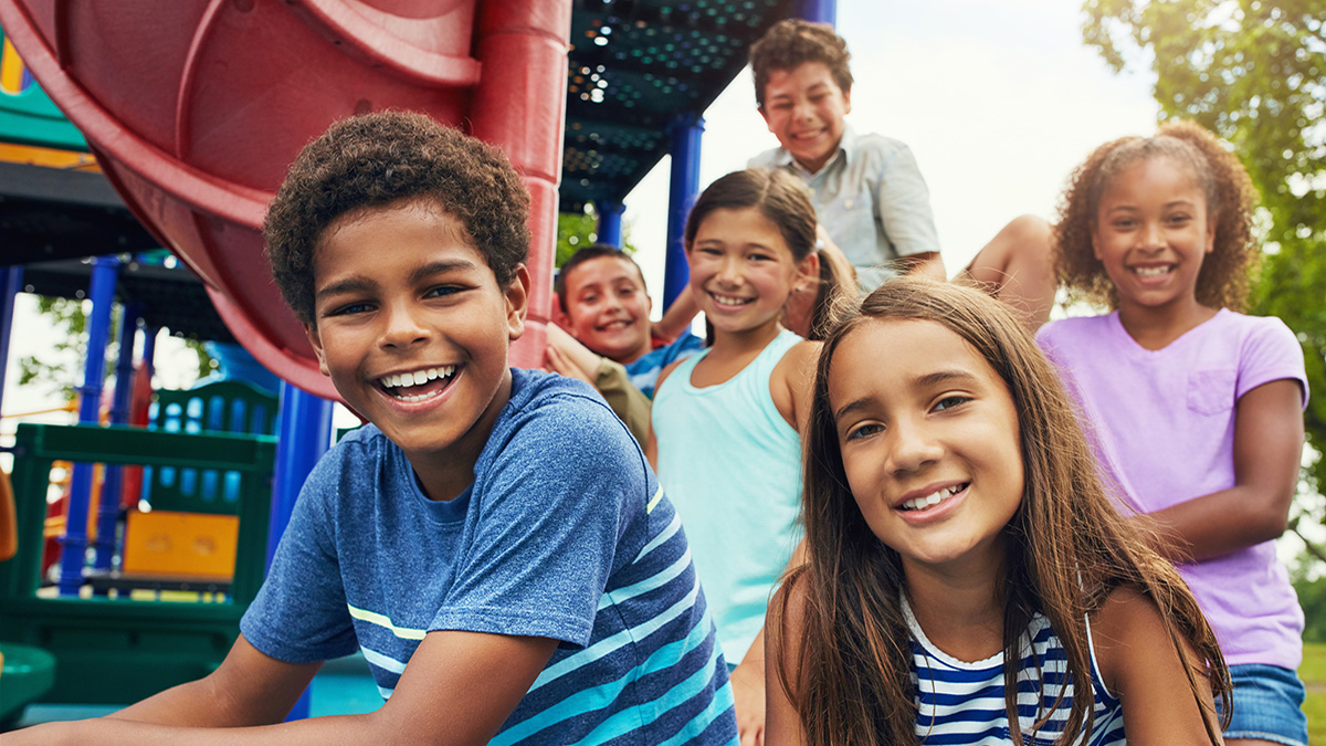 School aged children smiling while on a playground.