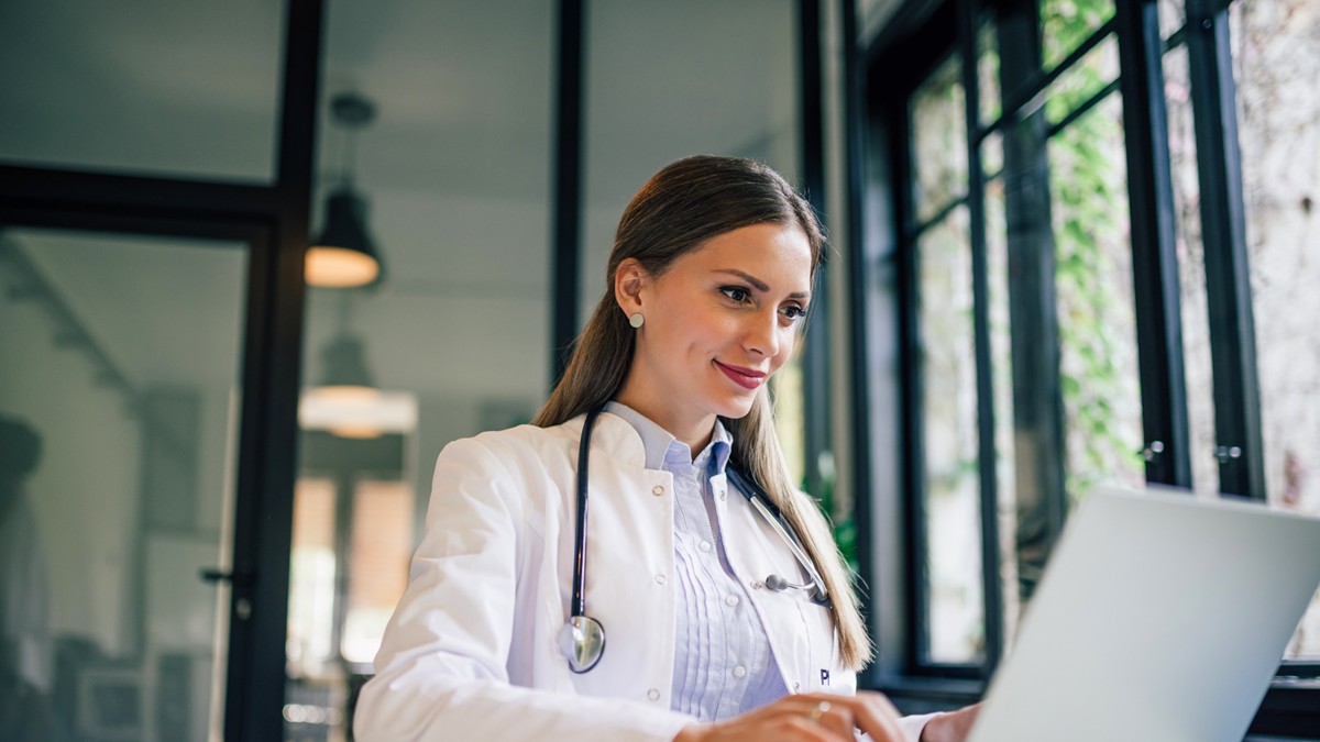 Una profesional de la salud sentada frente a su computadora y tomando un curso de educación continua.