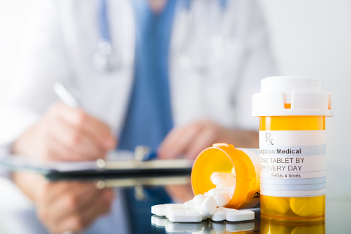 Doctor writes on a pad behind two bottles of pills
