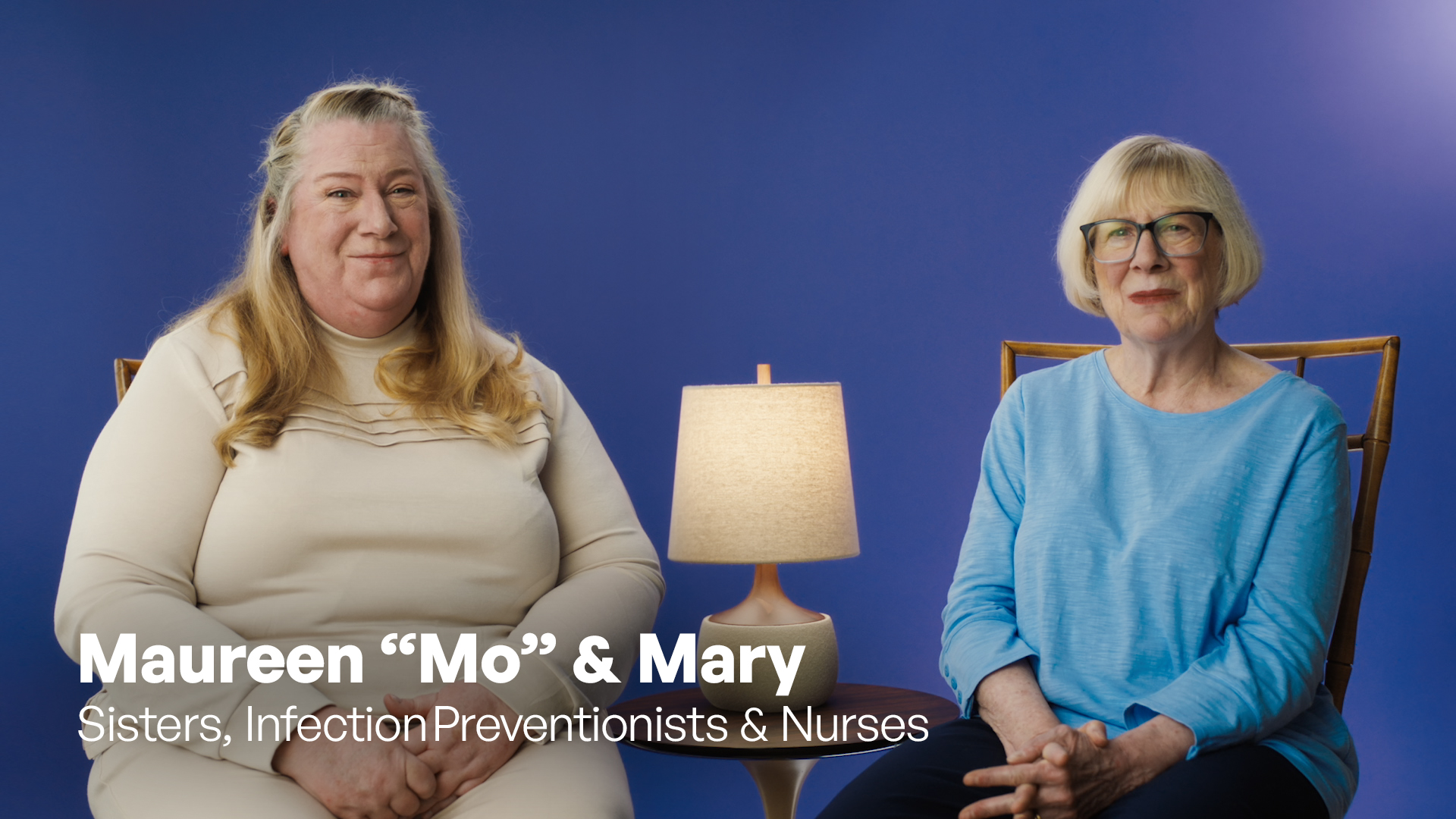 Mary & Mo Lansing are sisters, infection preventionists, & nurses. Mo & Mary are sitting in front of a blue background.