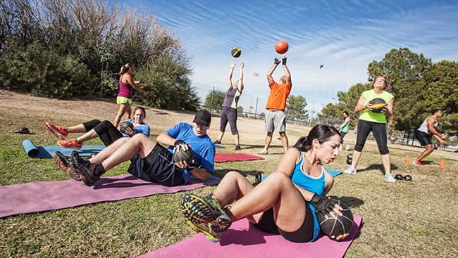 A group of teachers doing exercising and playing volleyball outdoors.