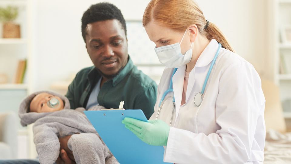 Father holding his newborn while talking to a healthcare provider.
