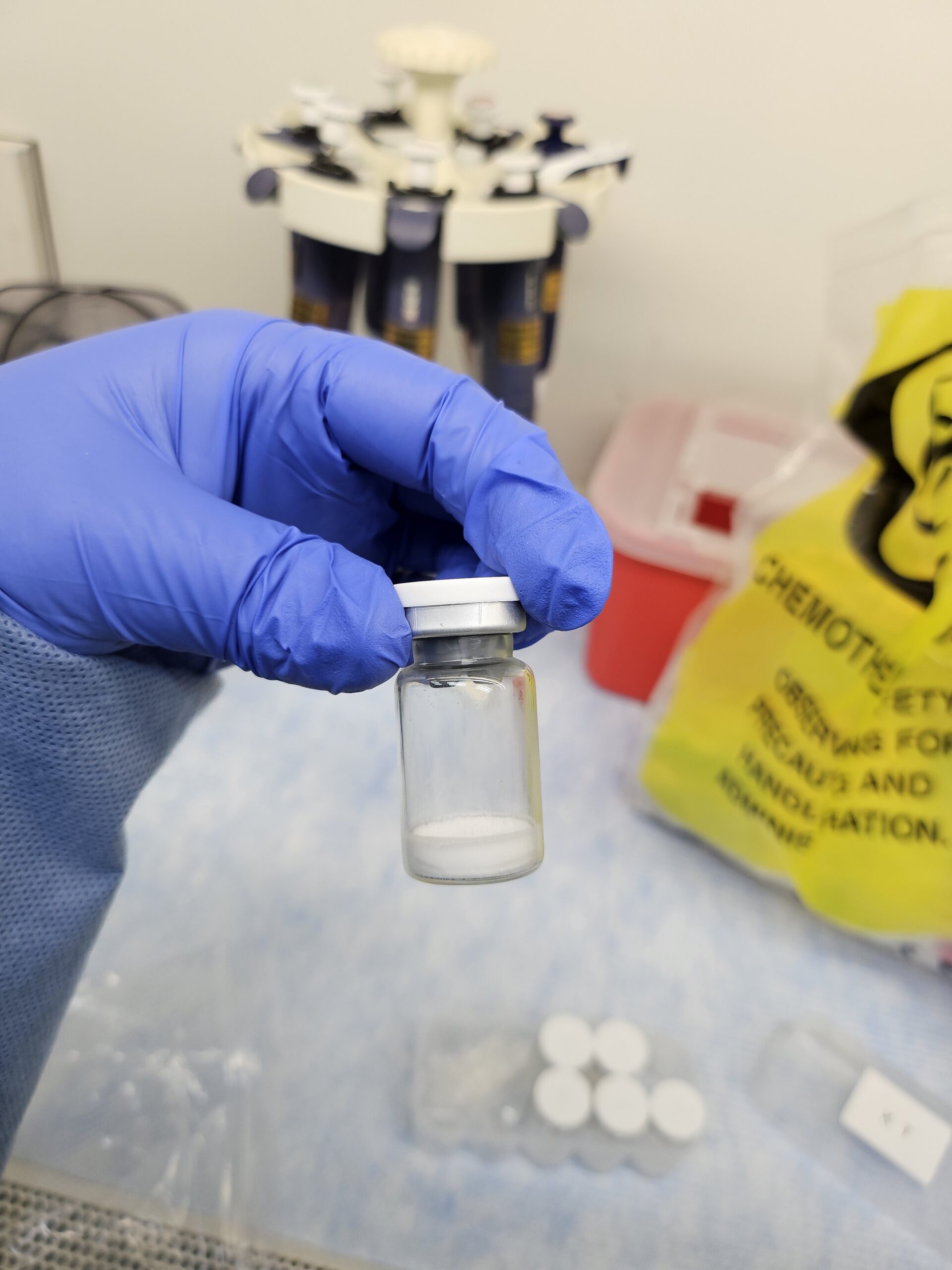 A gloved hand holding a clear vial containing white powder marketed as botulinum toxin for cosmetic injections.