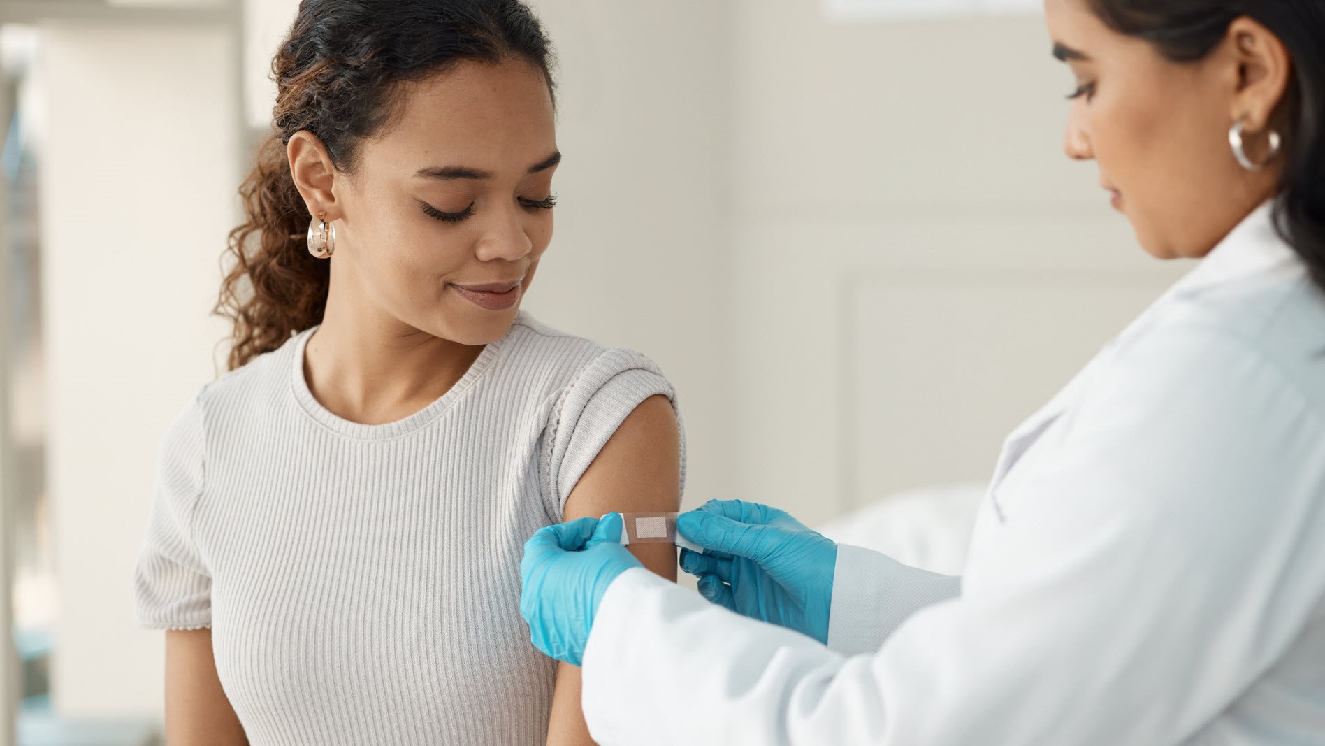 Doctor applying a band-aid after injecting her patient in the arm.