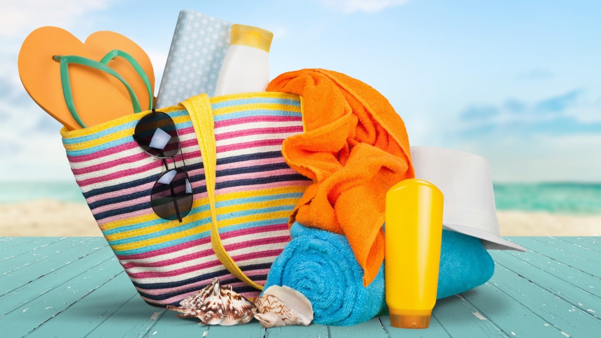 a colorful tote bag containing sunscreen, sunglasses, a hat, towels, and shoes