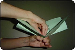 A person folds sheets of green paper to form a paper cabbage