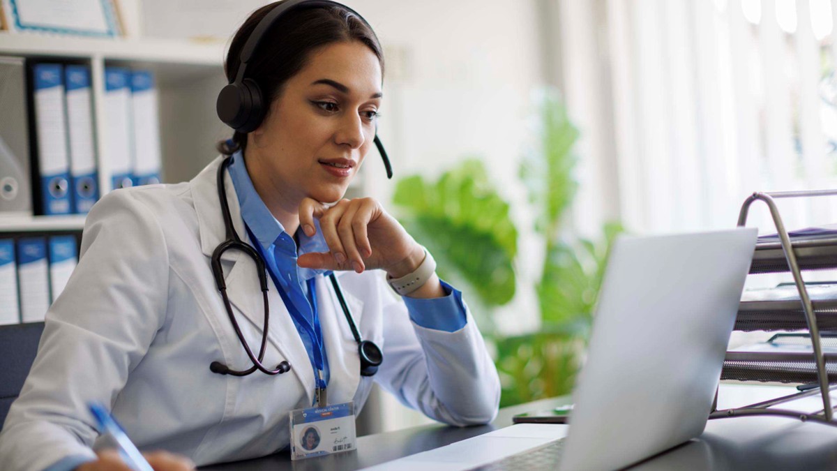 A female doctor takes an online clinical training using a headset and a laptop computer.
