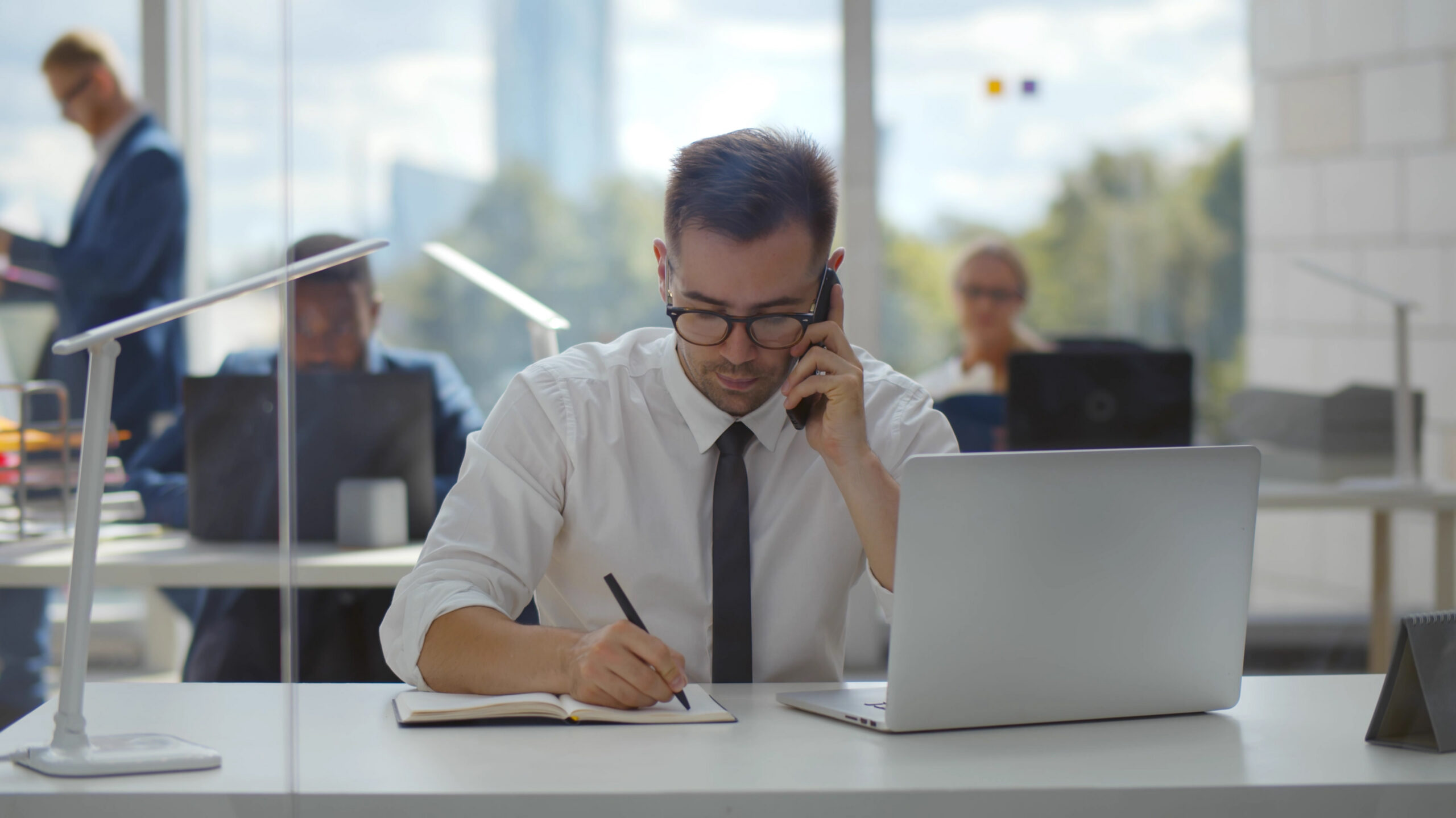A man writing note and on phone