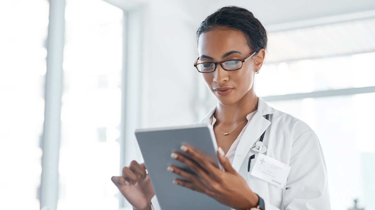 A HCP wearing glasses reads a tablet in an office.