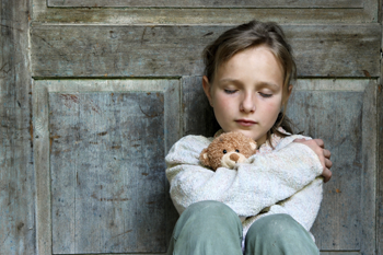 Young girl holding a teddy bear and looking sad