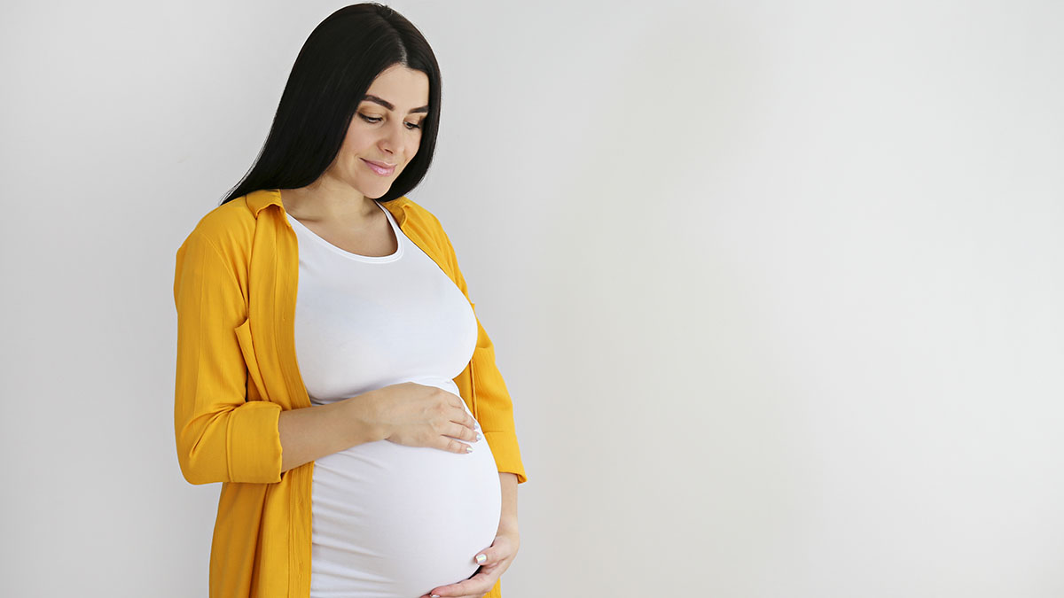 Pregnant woman with yellow shirt holding belly