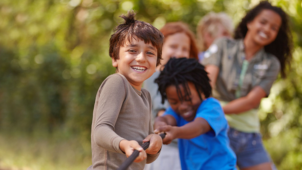 Children smiling and playing tug-of-war together outdoors on a sunny day.