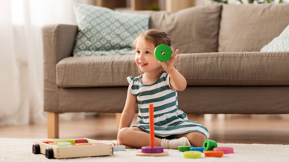 Niña sonriente sentada en el suelo, jugando con un juguete