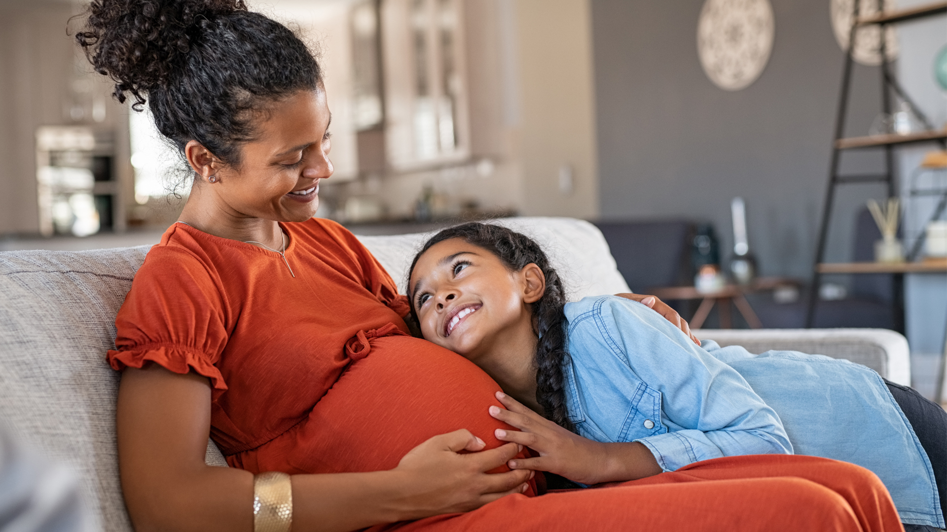 pregnant mother sitting on a couch with her young daughter sitting next to her with her head on her mothers lap