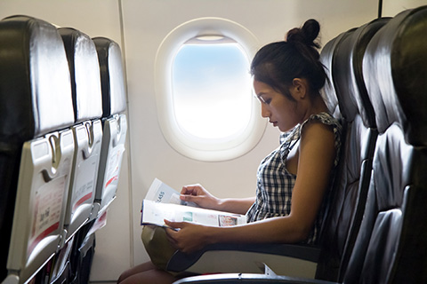 Mujer sentada en un avi&oacute;n mirando una revista