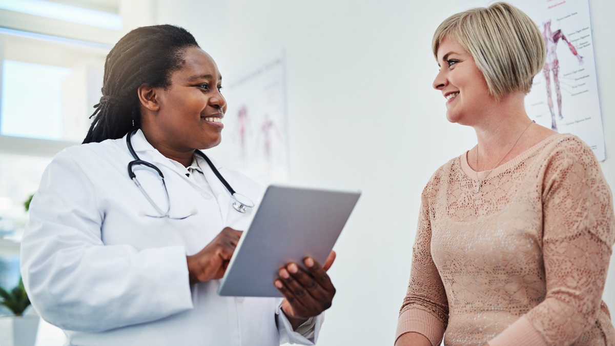 A doctor holding a tablet computer talks to her female patient