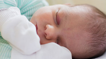 — title missing — Sleeping baby wearing mittens.