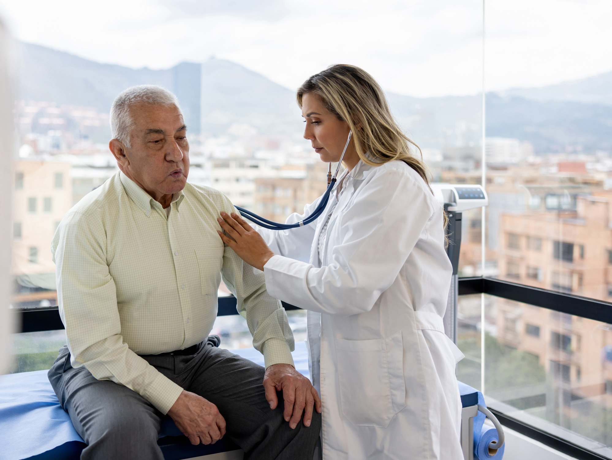 Patient examination A female healthcare provider using a stethoscope to examine an older man.