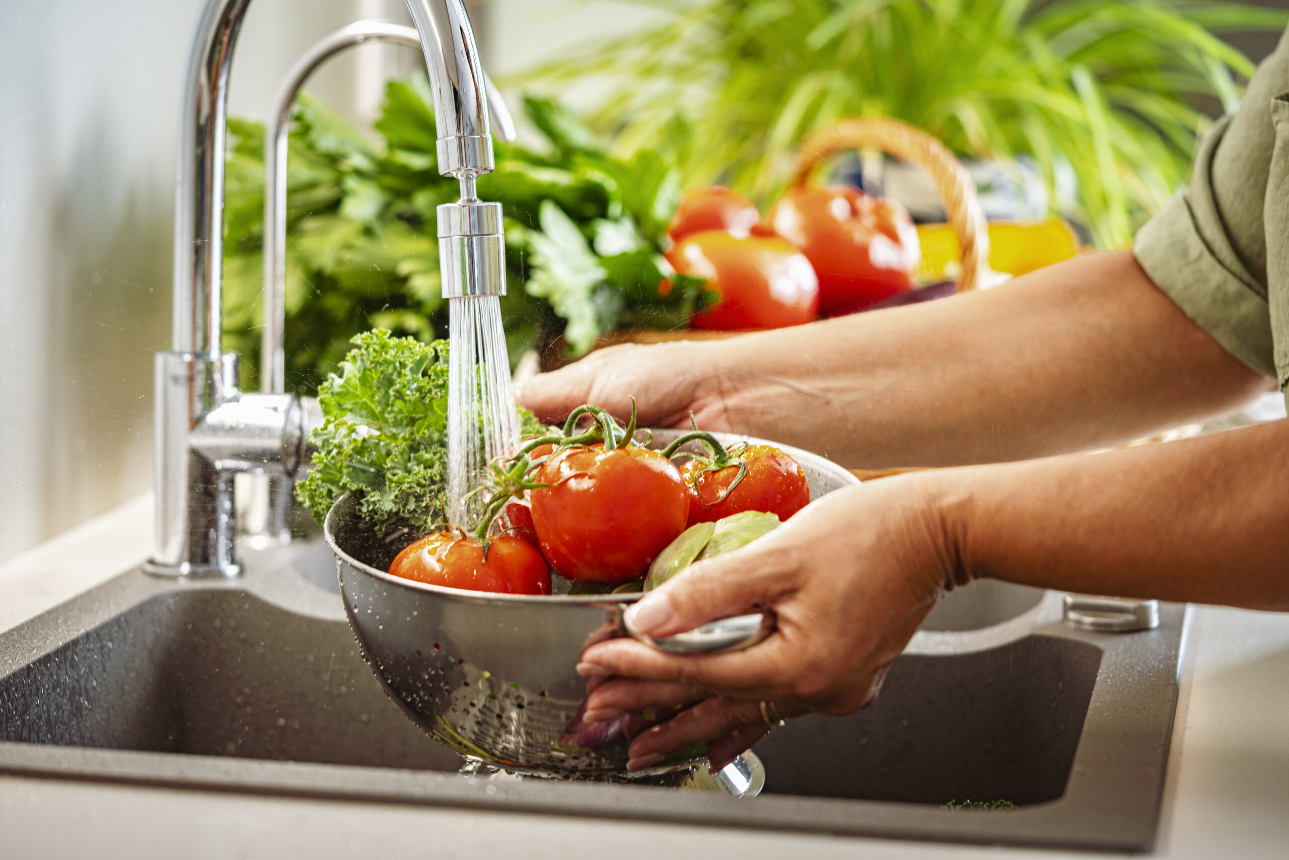 Person rinsing vegetables under faucet.