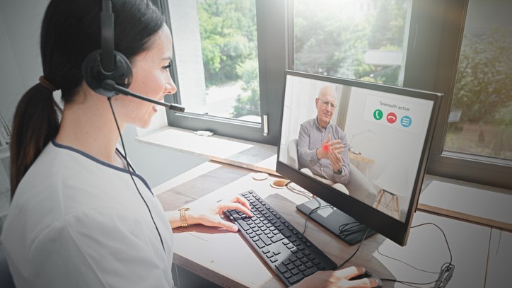 Woman with headset having a telehealth visit with a man using a laptop.