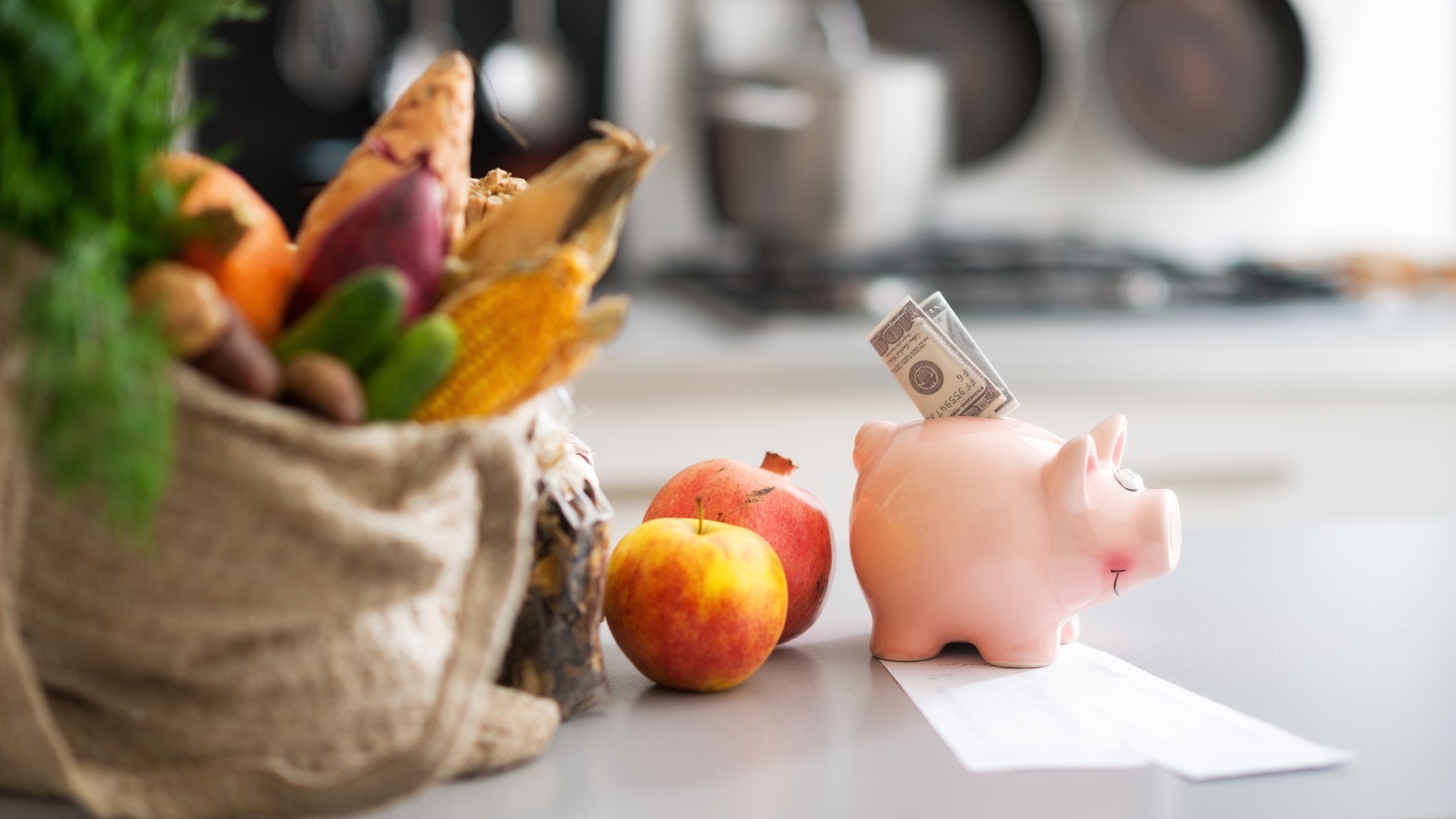 Dinero dentro de una alcanc&iacute;a y una compra de alimentos sobre una mesa.