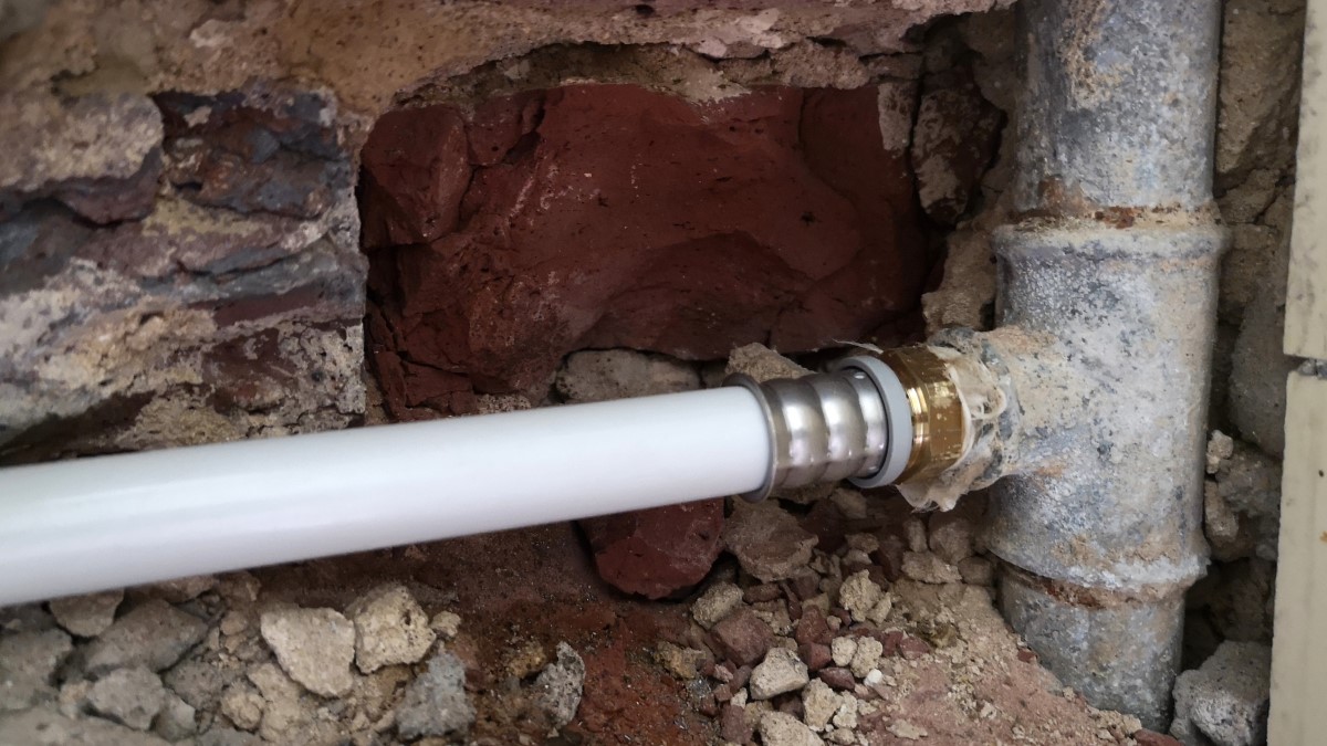 Tubería de agua de metal vieja en la pared conectada a una tubería de plástico
