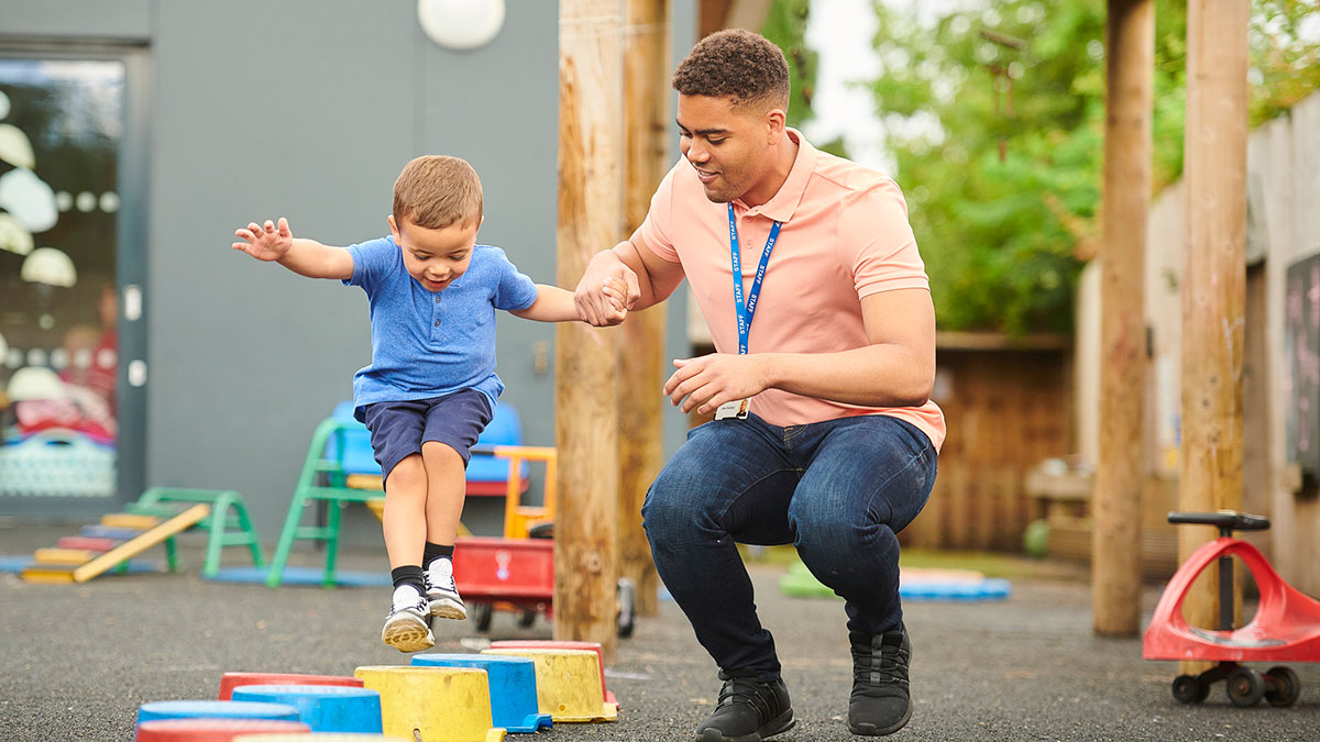 An early educator helping a child jump on the playground.