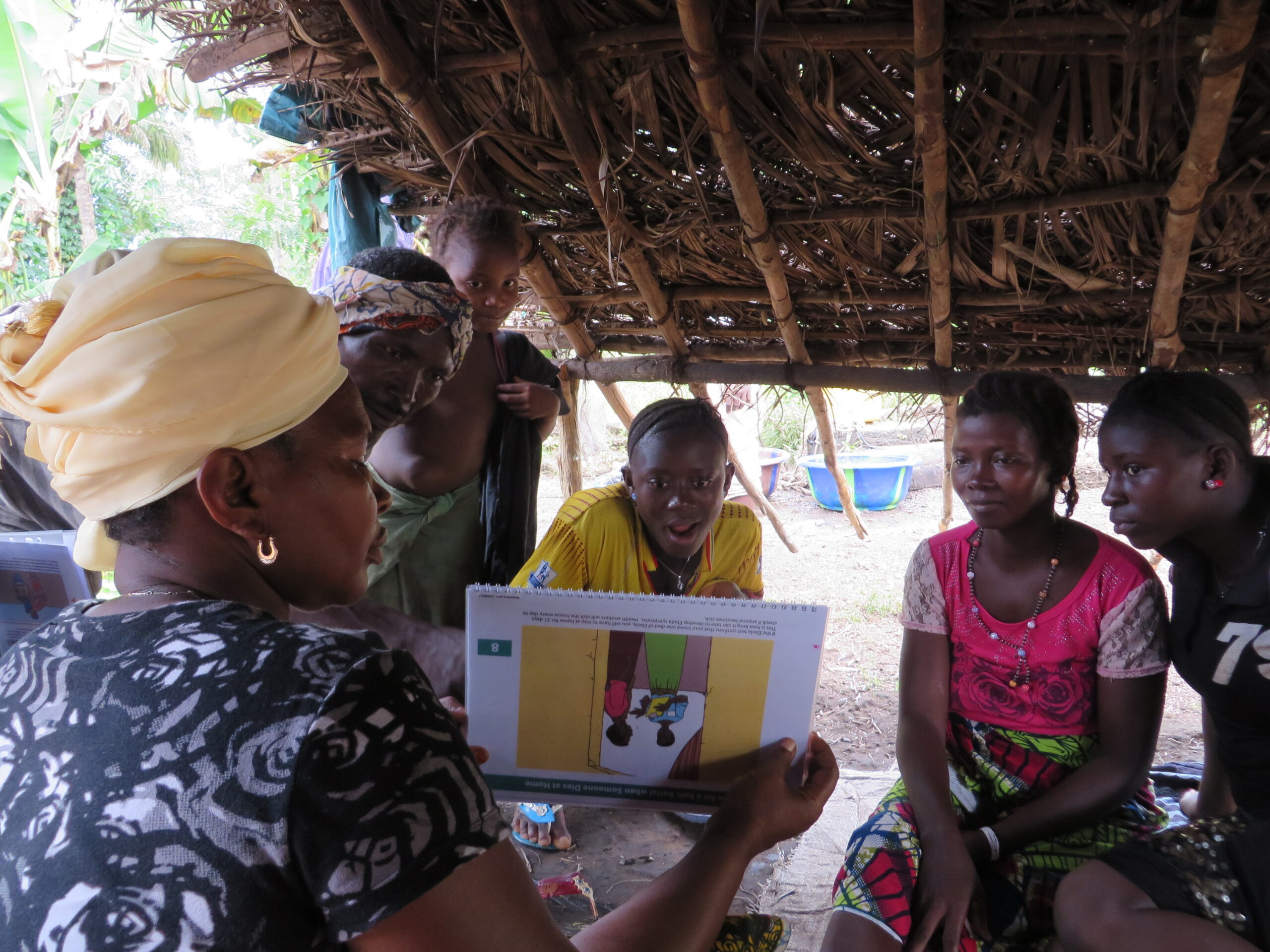A community health worker shows an educational flipbook to a group of people.