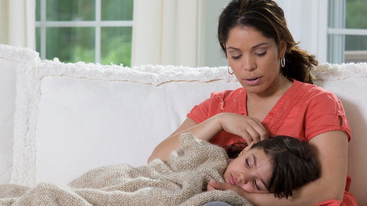 A woman on a couch holds and comforts a young boy who is not feeling well.