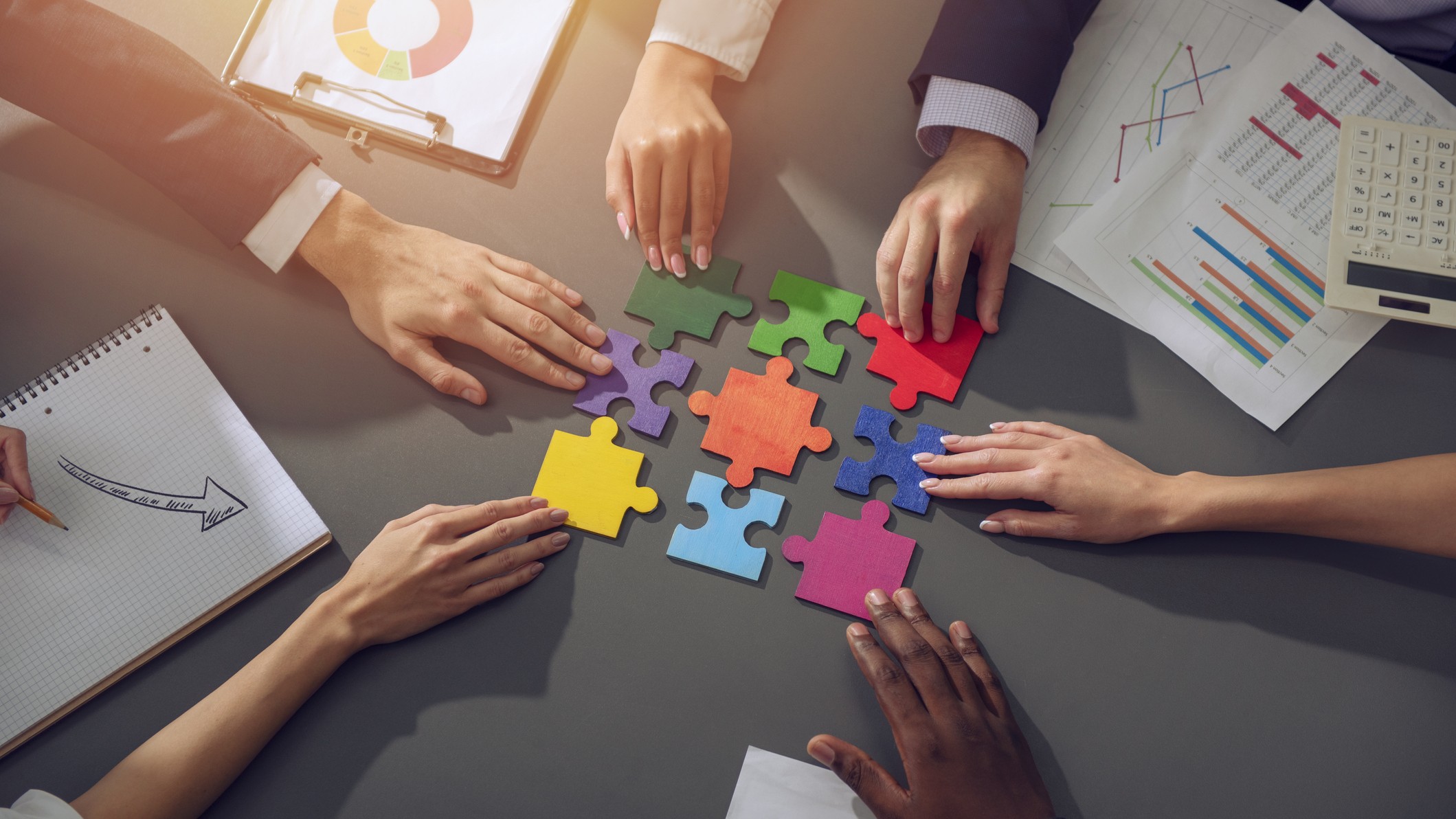 Professionals working together, reaching their hands in to collectively put the puzzle pieces together.