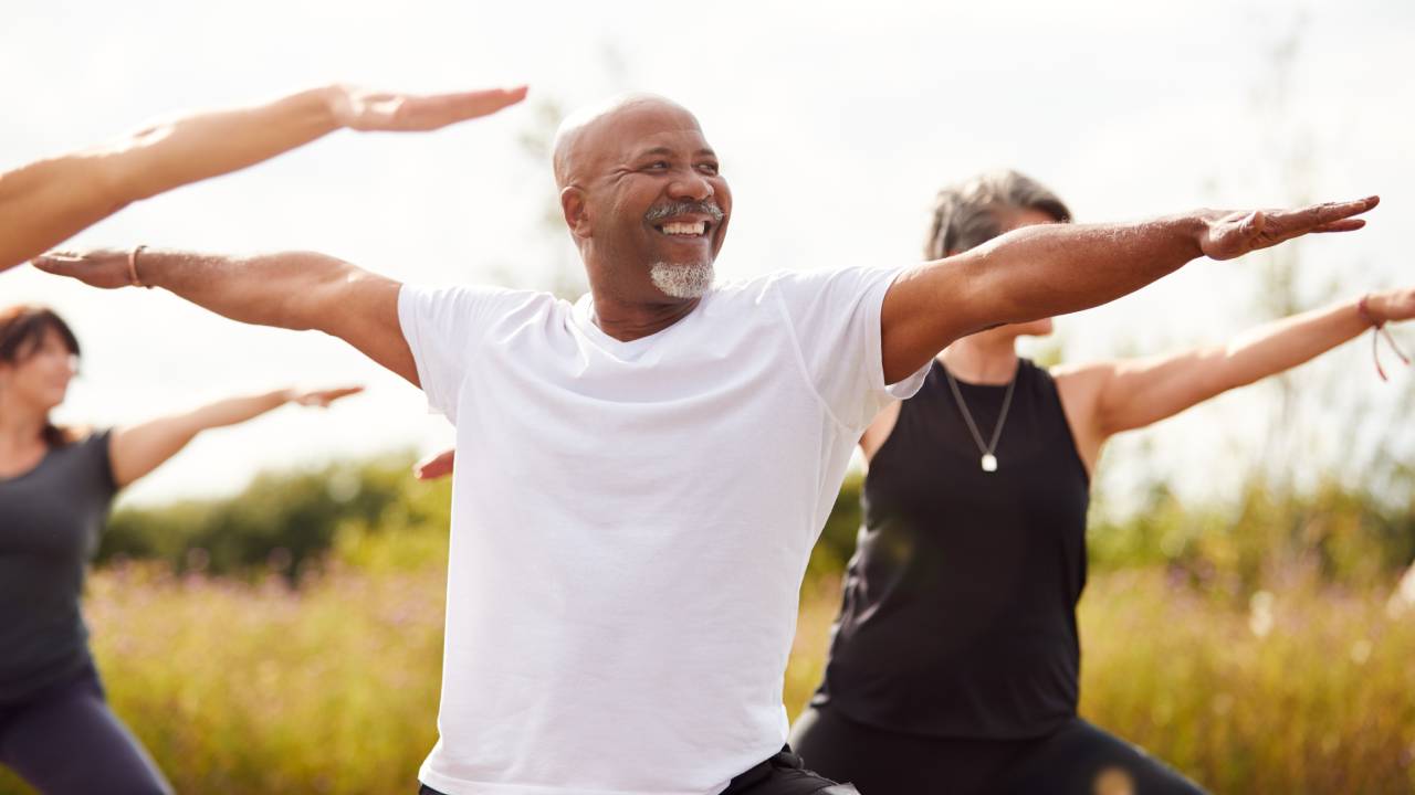 Man in white shirt in "warrior" yoga pose flanked by two workout participants