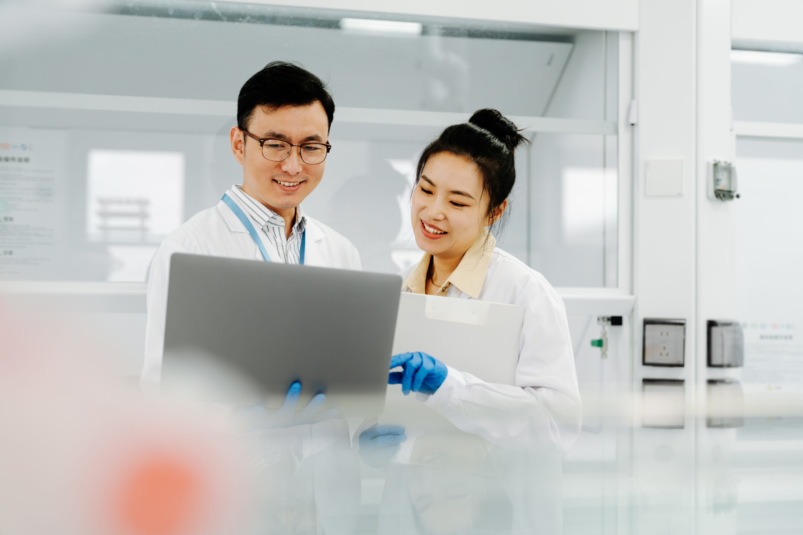 Two laboratorians looking at a laptop in front of a fume hood.