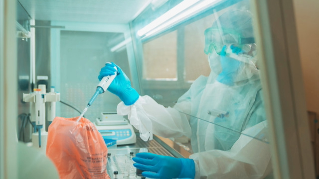 Person wearing personal protective equipment in a lab setting holding lab equipment.