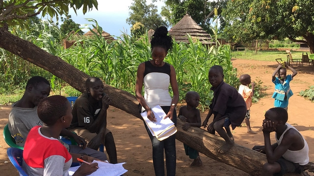 Group with men, a woman, and children in a field standing in the dirt.