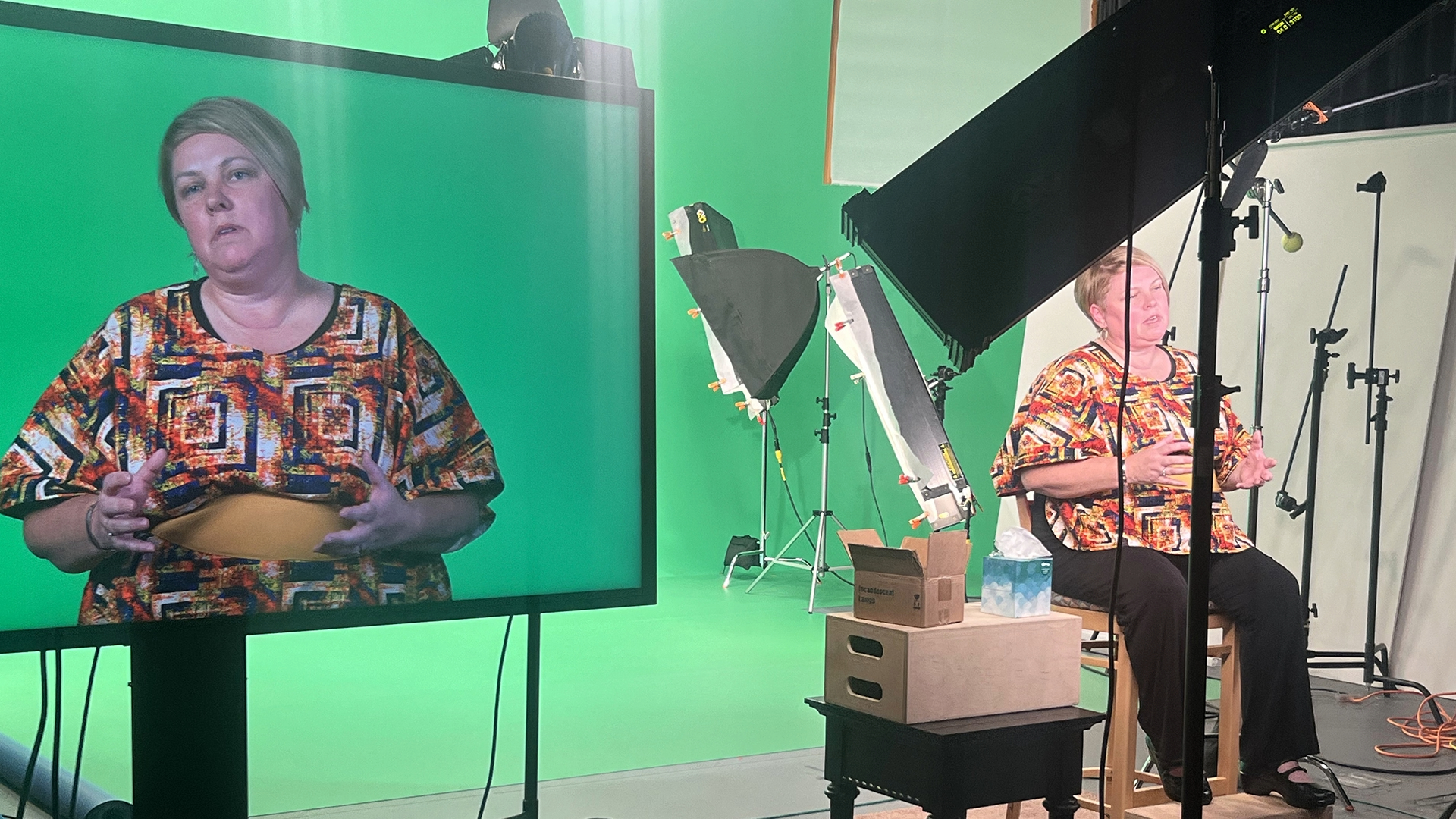 A woman in a studio sitting in front of a green screen being recorded.
