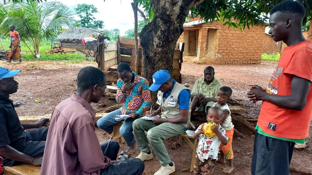 Group of adults, one writing on a clipboard, and children in a rural setting in Guinea