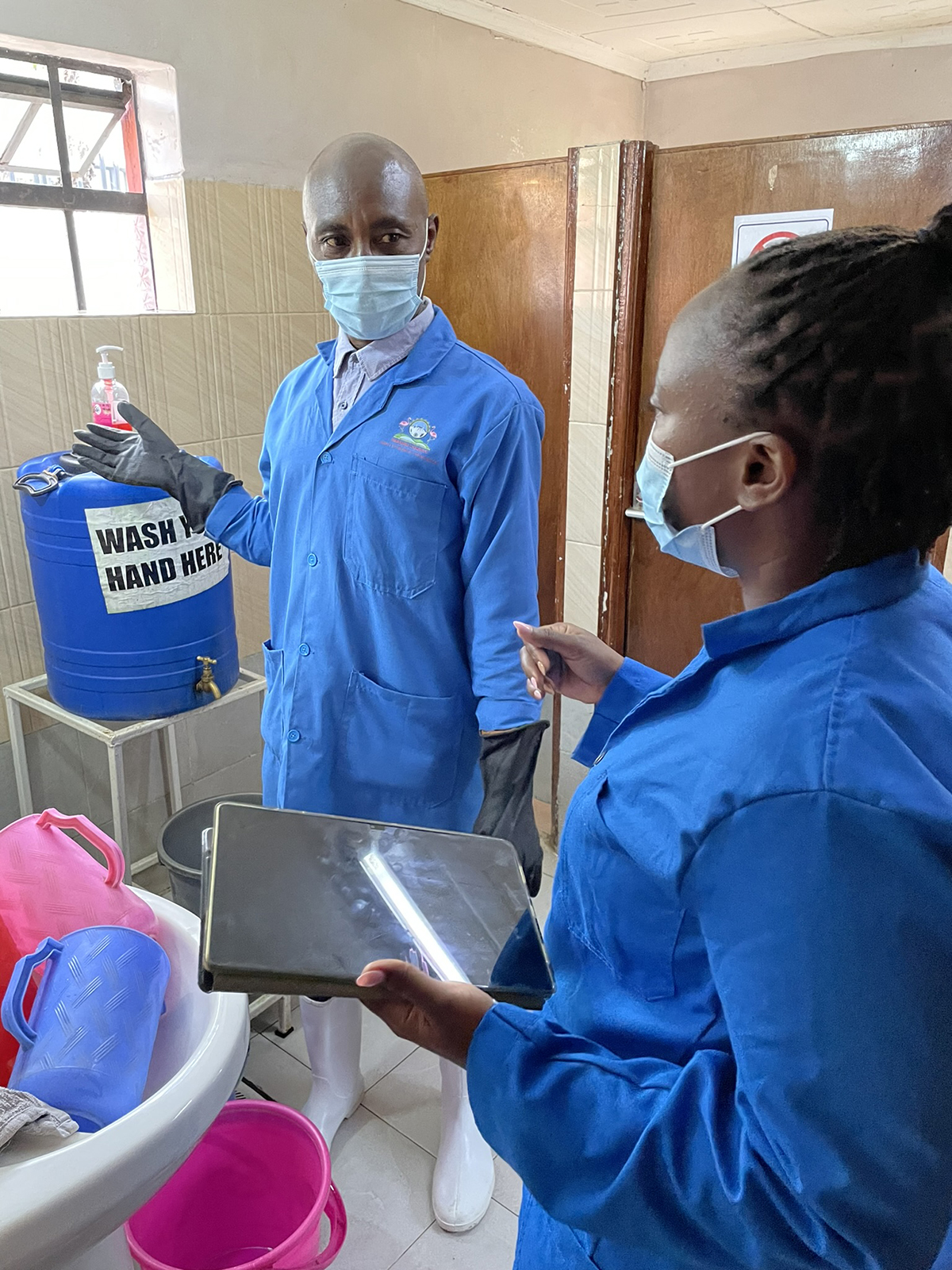 Evaluator Alice Arondo observes Solomon Mwangi preparing a disinfectant solution used to clean toilets.