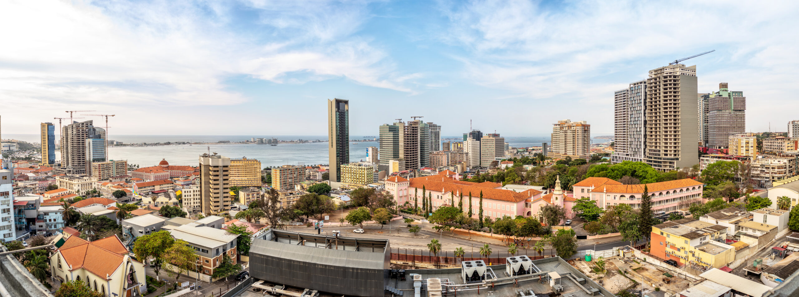 Panoramic daytime photograph of the city of Luanda, Angola, with the bay in the background, roads, and high-rise buildings.
