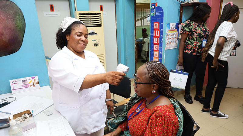 A woman has her temperature checked by a nurse at a healthcare facility in Nigeria.