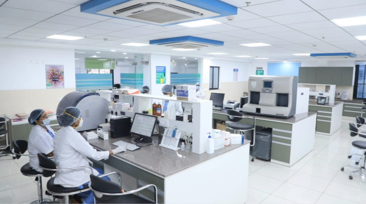 Medical laboratory with staff in protective gear working at counters with diagnostic equipment and computers.