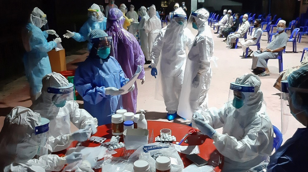 Health care workers in protective gear and individuals sitting down waiting to be seen.