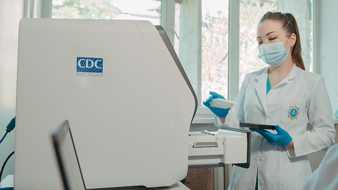 Woman wearing mask in lab setting, standing in front of equipment