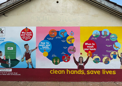 Mural on school building titled clean hands save lives illustrates handwashing steps and encourages students to practice hand hygiene.