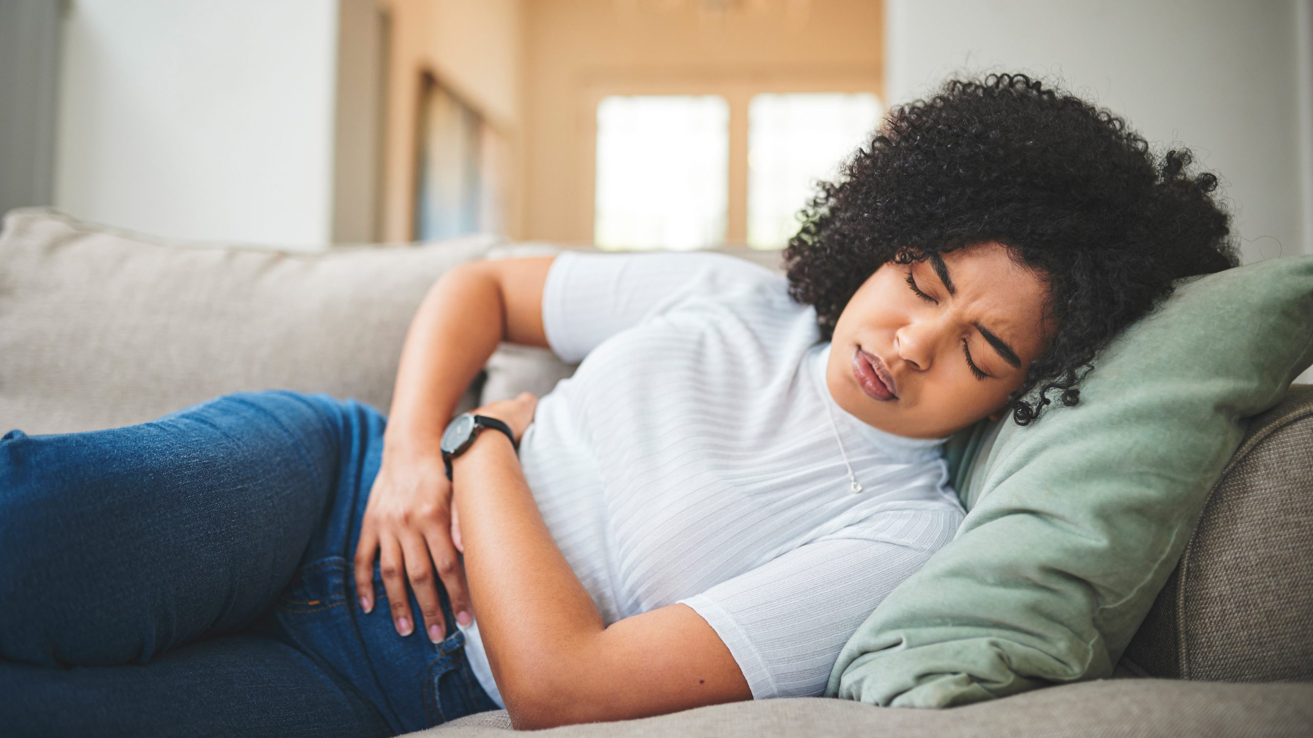 Woman holding stomach A young woman lays on a couch holding her stomach in pain