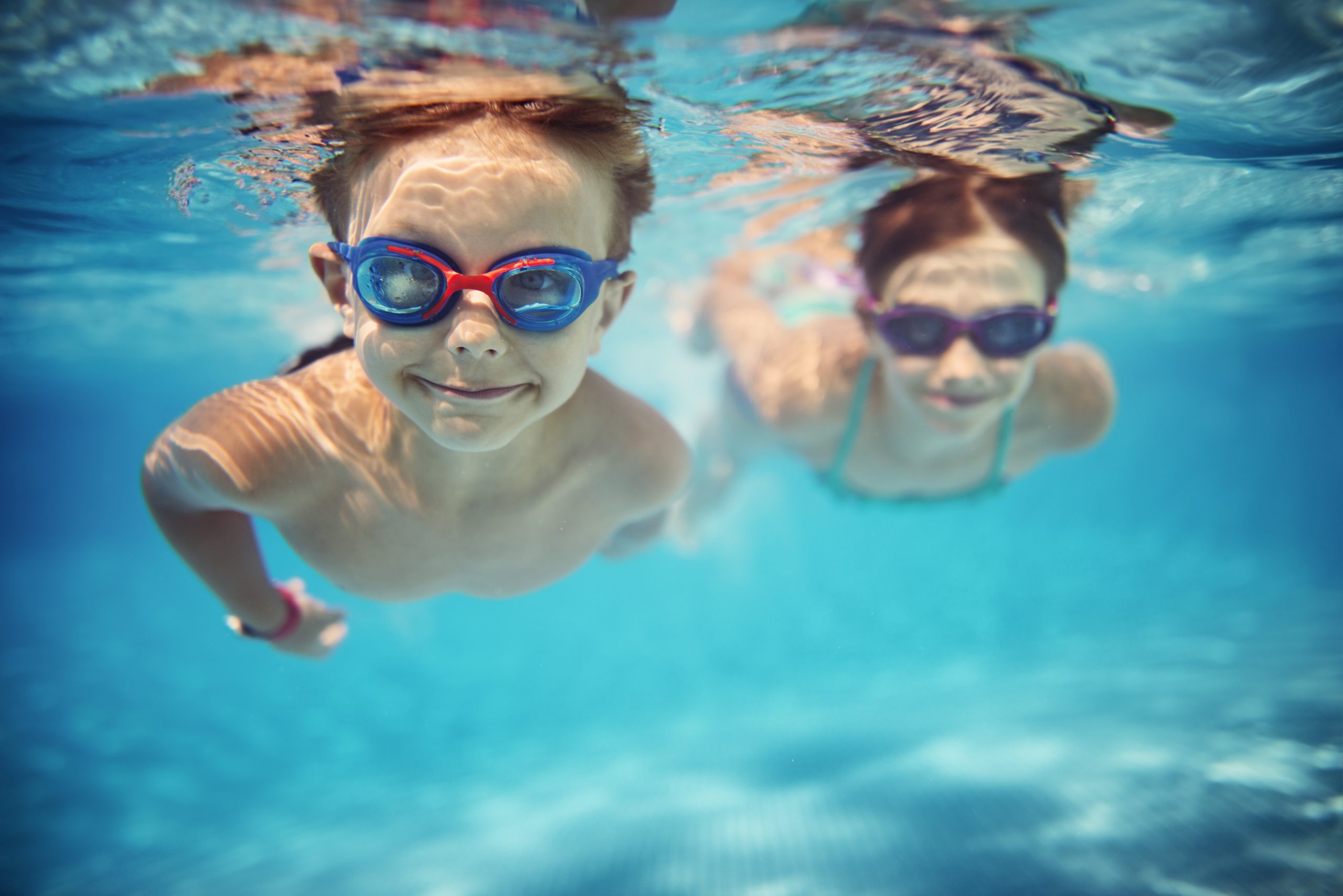 Two young boys swimming in a pool under water wearing goggles